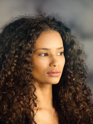 Headshot of a beautiful thoughtful black girl with long curly hair looking off to the side with a pensive serious expression