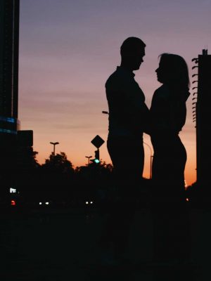Silhouette of young happy couple in love kissing on city street at the sunset